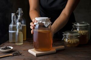 Person holding a jar of kombucha with other fermentation jars and bottles on a wooden table.