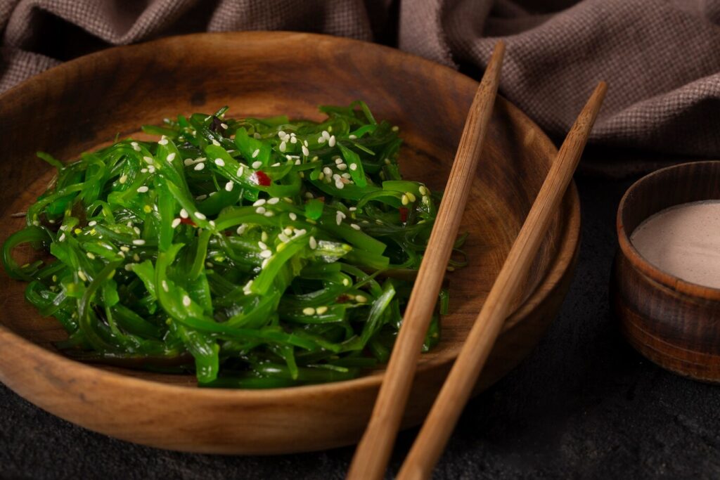 A wooden bowl of vibrant green seaweed salad topped with sesame seeds