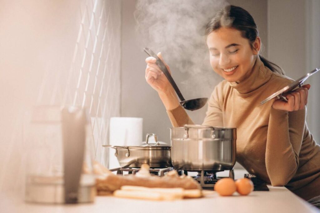 A person stirs a pot on the stove, surrounded by steam, with eggs and ginger