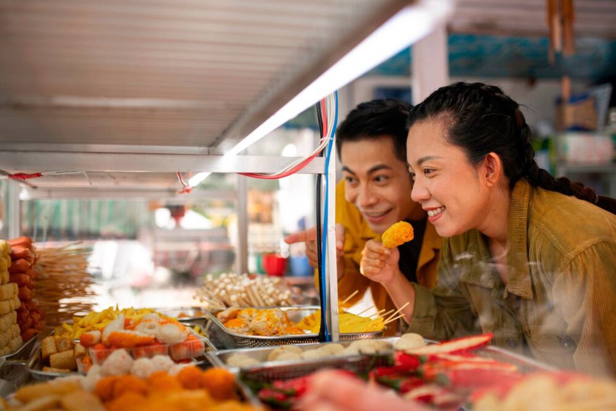 A smiling couple choosing street food from a colorful outdoor stall.