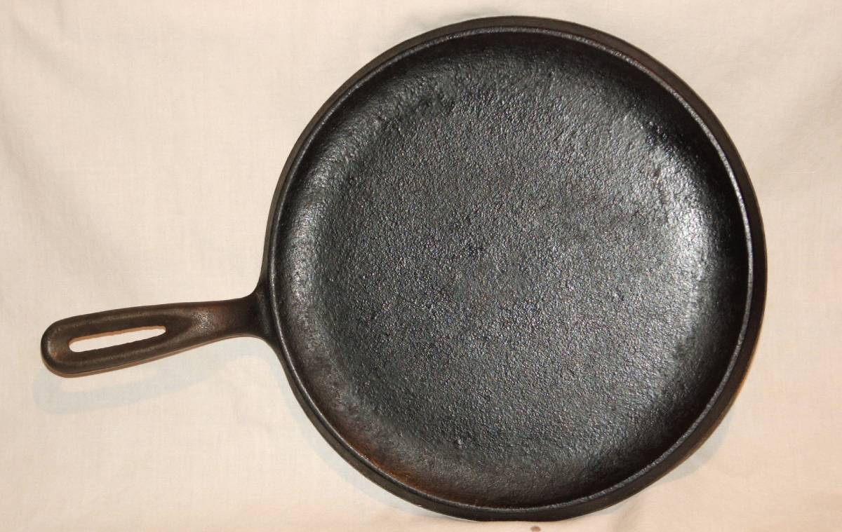 Top view of a cast iron skillet with a smooth, dark surface and a sturdy handle, set against a light fabric background.