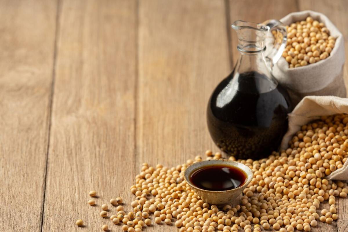 Soybeans in a sack with a small bowl and jug of soy sauce on a wooden table.