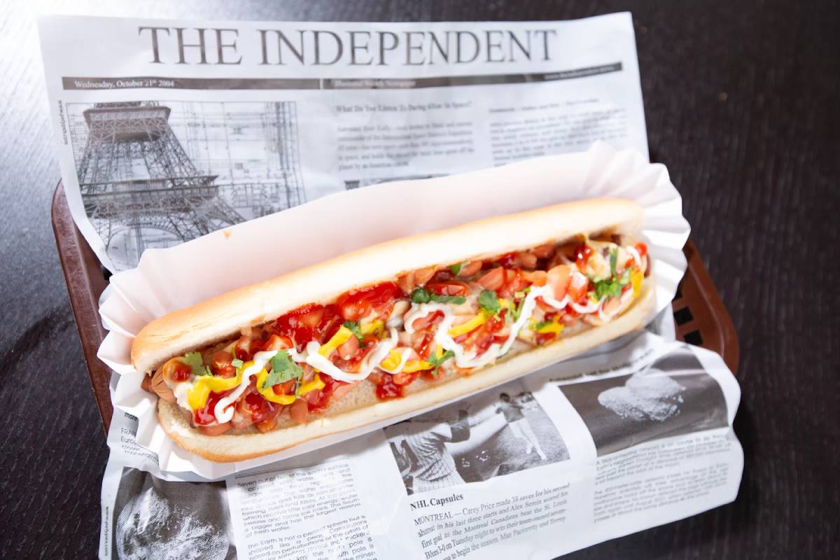 A colorful hot dog topped with ketchup, mustard, mayo, and veggies sits on a newspaper tray, capturing a casual dining moment.