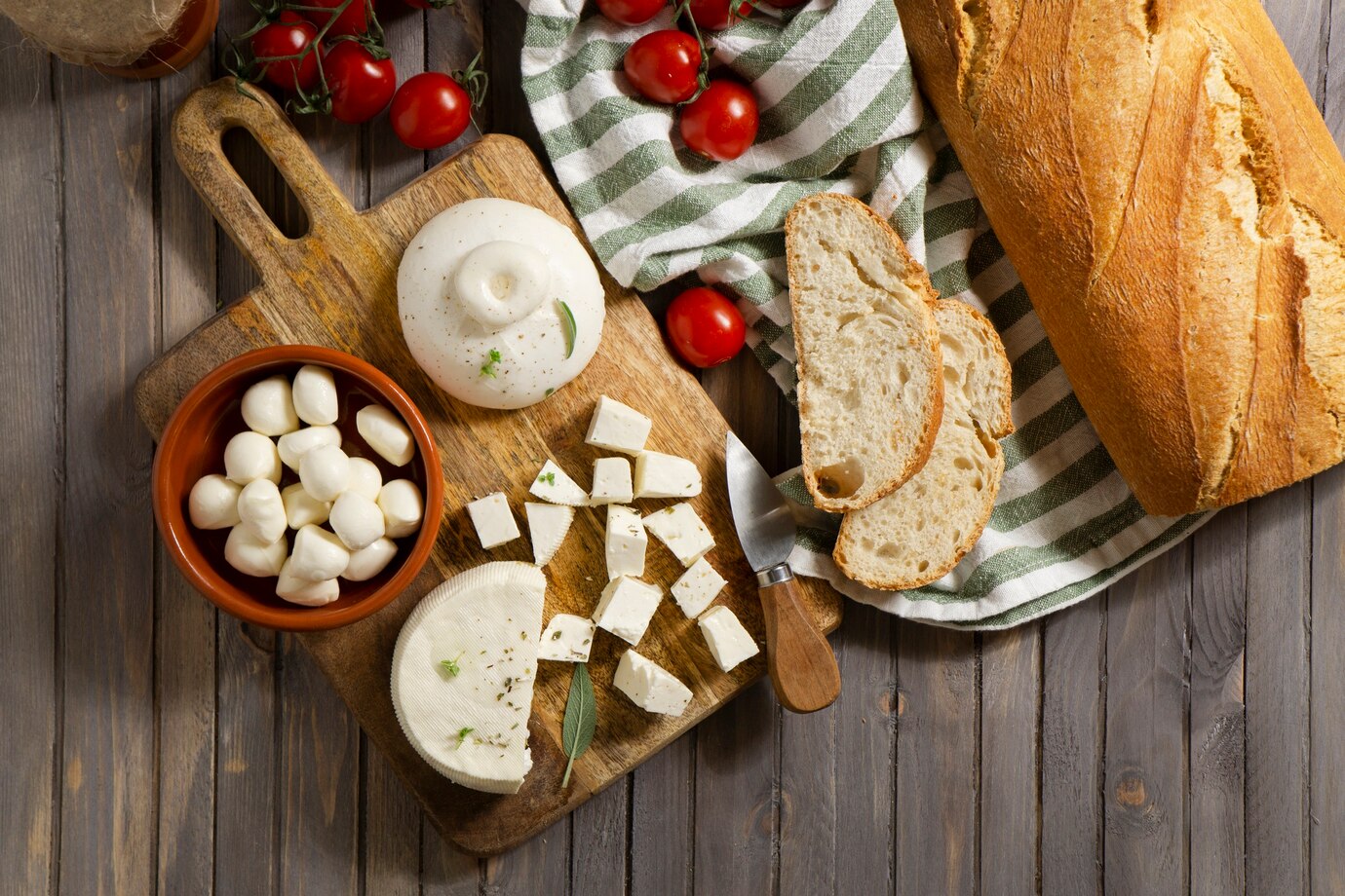 A wooden cutting board displays mozzarella, burrata, and feta cheeses