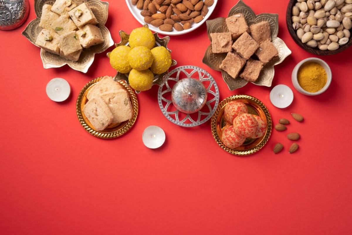 An assortment of traditional Indian sweets and nuts arranged on a red background.