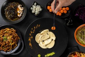 Assorted Asian dishes displayed on a dark table, with a person using chopsticks to pick up a carrot.