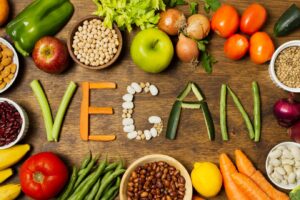 Assorted fresh vegetables and legumes on a wooden surface spelling "VEGAN."