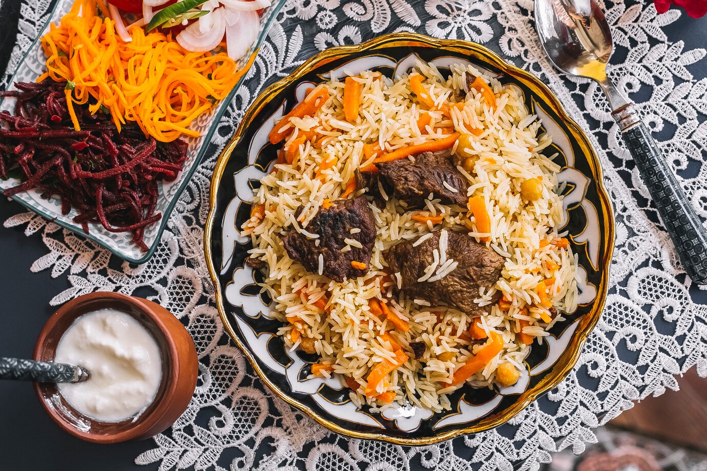 A colorful plate of rice with tender meat pieces and carrots, surrounded by salads