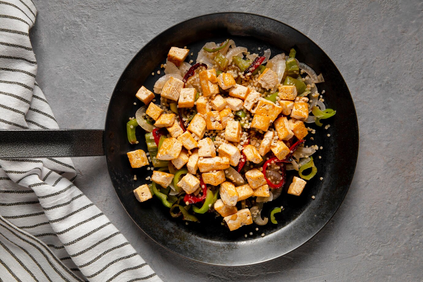 A skillet filled with sautéed tofu cubes, mixed with colorful peppers and onions