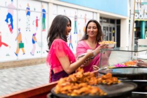 Two women in traditional Indian attire selecting food at a street market stall.