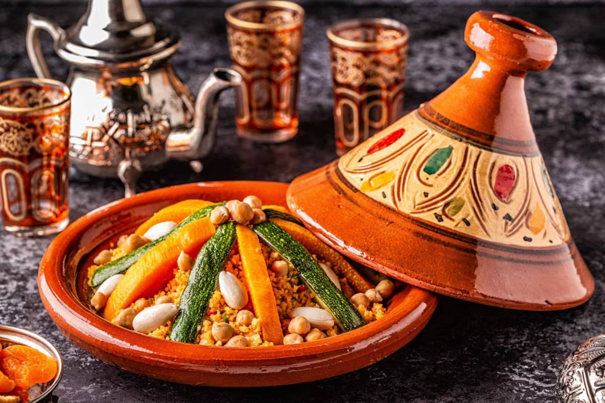 Two traditional Moroccan tagines sit on a wooden table, surrounded by glassware and plates, ready for a communal meal.