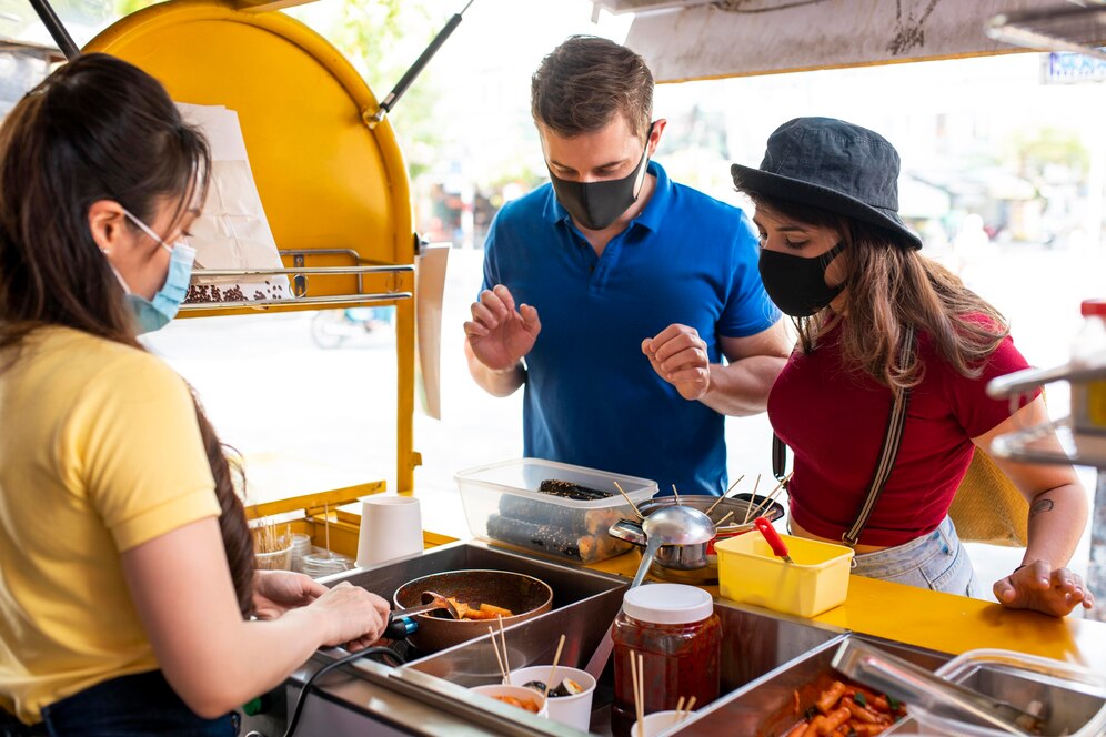 A woman serves food to customers wearing masks at a street food stall.