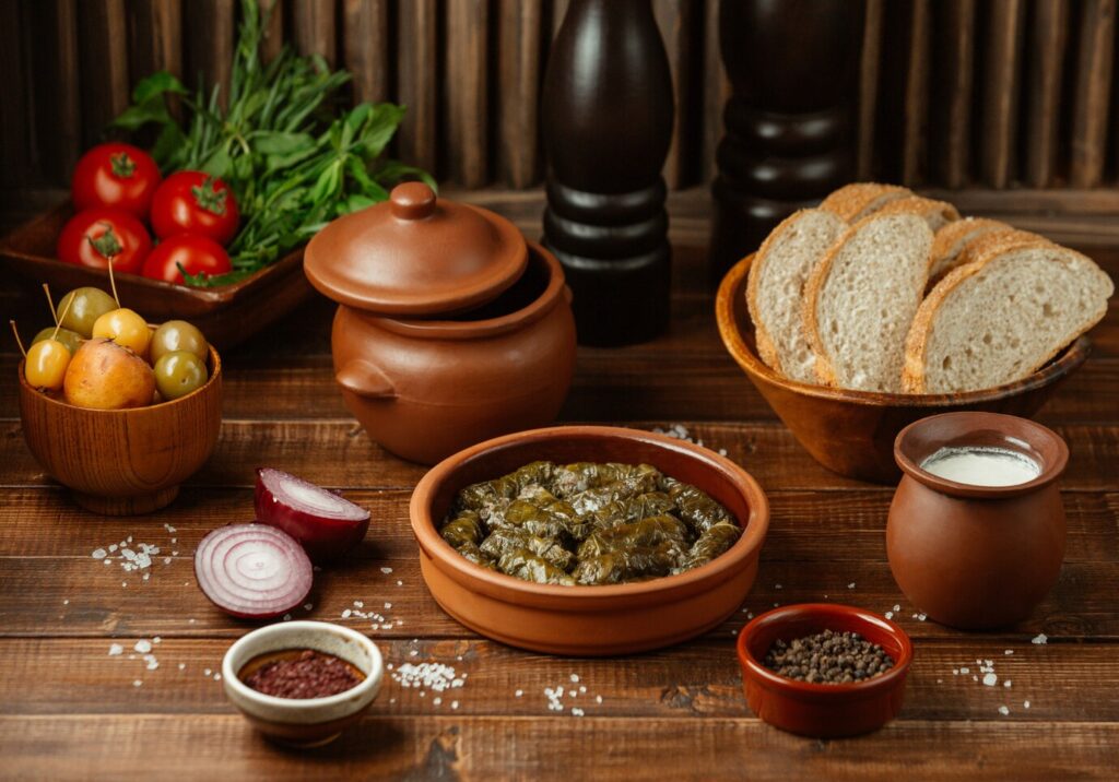 Traditional meal setup with stuffed grape leaves, fresh vegetables, bread, and pottery dishes on a wooden table.