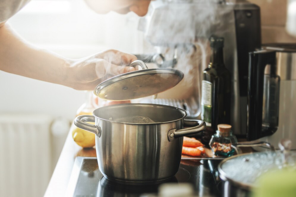 Person cooking, lifting lid off a steamy pot on a stove in a home kitchen.