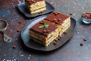 Two slices of layered tiramisu cake with coffee beans and powdered sugar, on dark plates against a starry background.