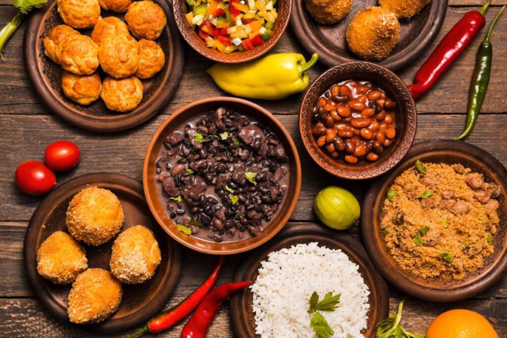Assorted traditional Brazilian dishes including beans, rice, farofa, and acarajé on a wooden table with fresh chili peppers.