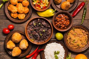 Assorted traditional Brazilian dishes including beans, rice, farofa, and acarajé on a wooden table with fresh chili peppers.