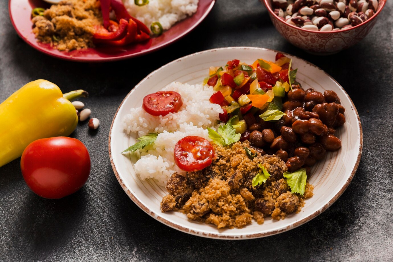 A plate of rice with tomatoes, mixed bell peppers, beans, and spiced ground meat, surrounded by fresh vegetables.