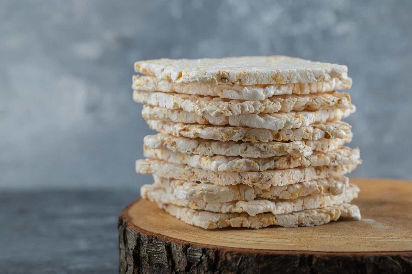 A stack of rice cakes sits on a wooden surface, with a blurred gray background
