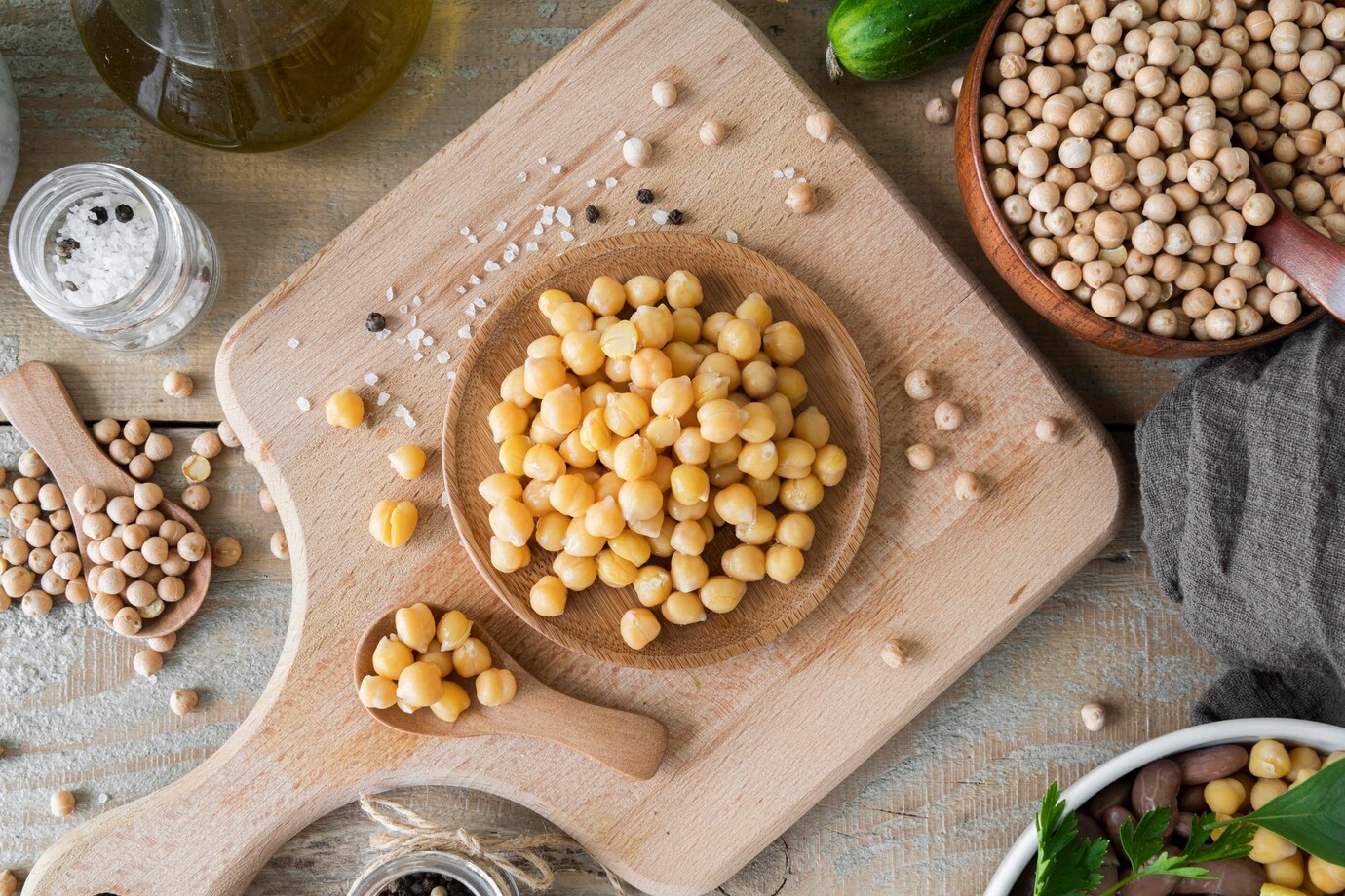 A wooden board filled with chickpeas, salt, and spices, surrounded by a bowl 