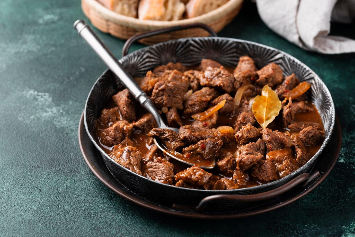 A close-up of a savory beef stew in a decorative black bowl, garnished with bay leaves