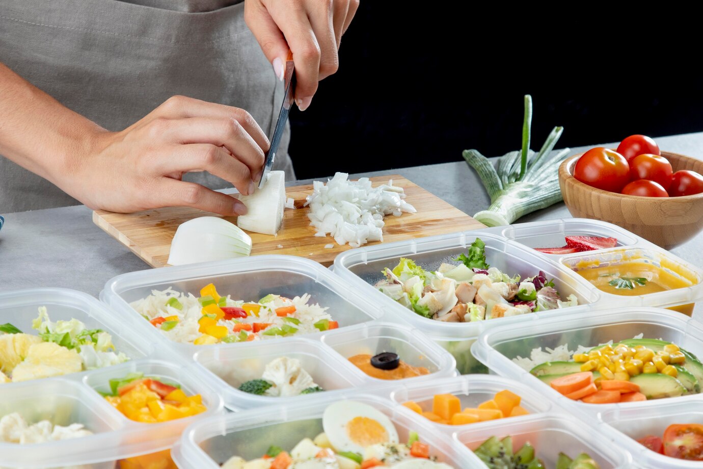 Person chopping an onion with various prepped meals in containers on a kitchen counter.