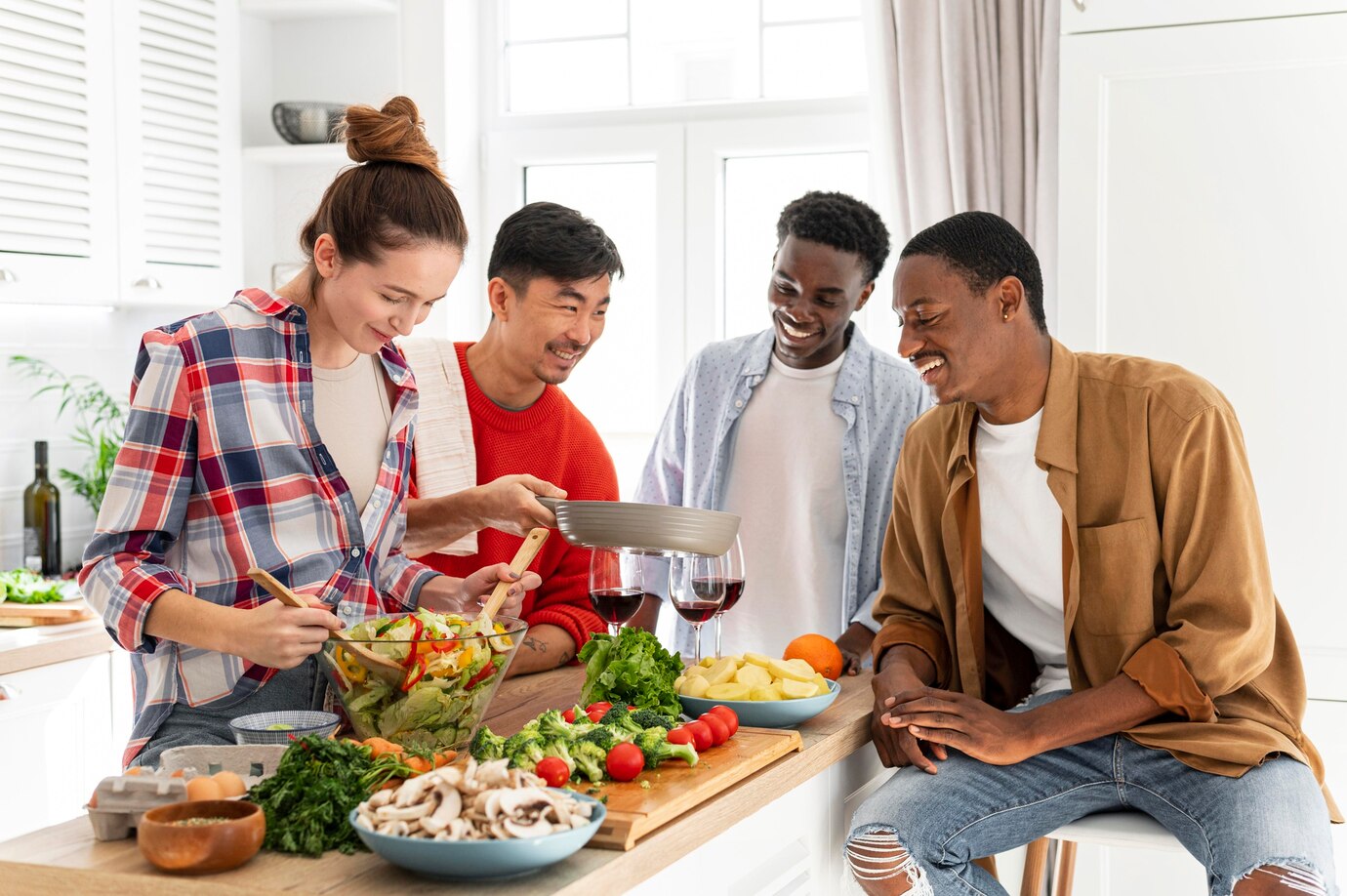Four diverse friends laughing and preparing food together in a modern kitchen.