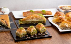 Assorted traditional Middle Eastern pastries on plates, including baklava and pies topped with pistachios.