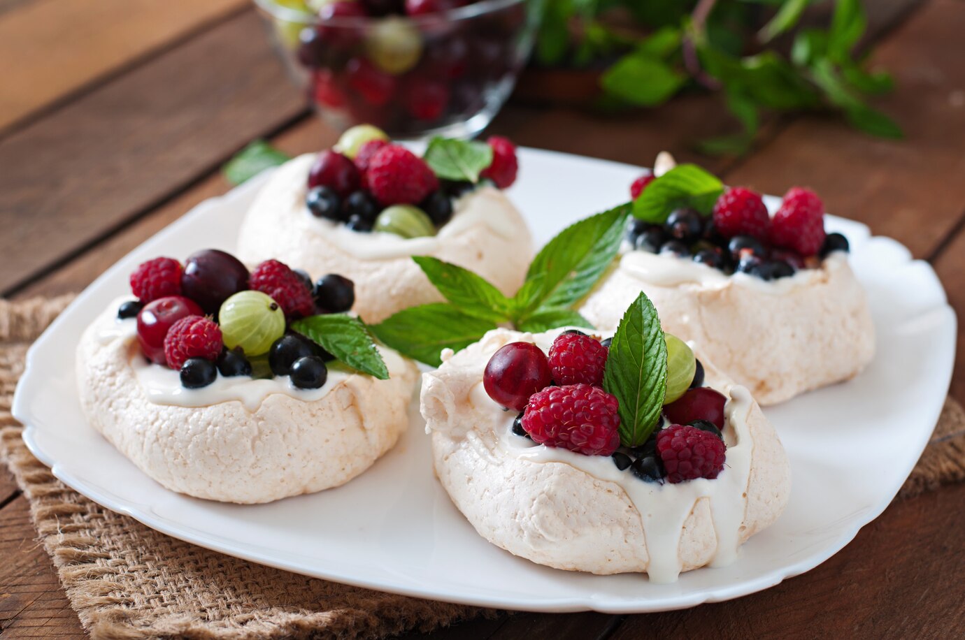 Four meringue nests topped with whipped cream and a variety of fresh berries
