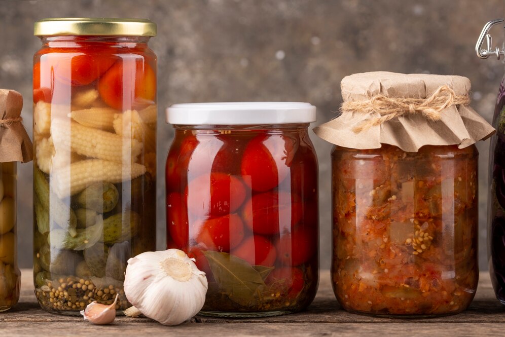 Assorted pickled vegetables in glass jars on a wooden table.