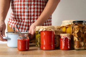 Person in plaid shirt canning homemade pickles and sauces at kitchen counter.