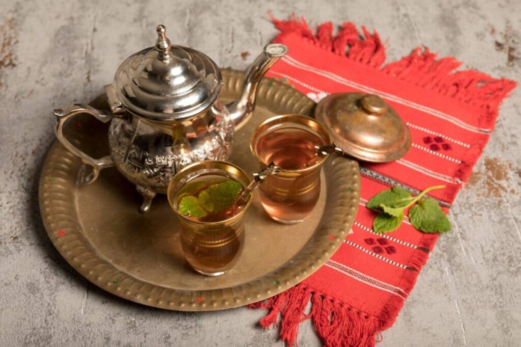 Traditional Moroccan tea set on a tray with two glasses of tea, on a red textile.