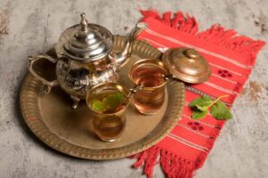 Traditional Moroccan tea set on a tray with two glasses of tea, on a red textile.