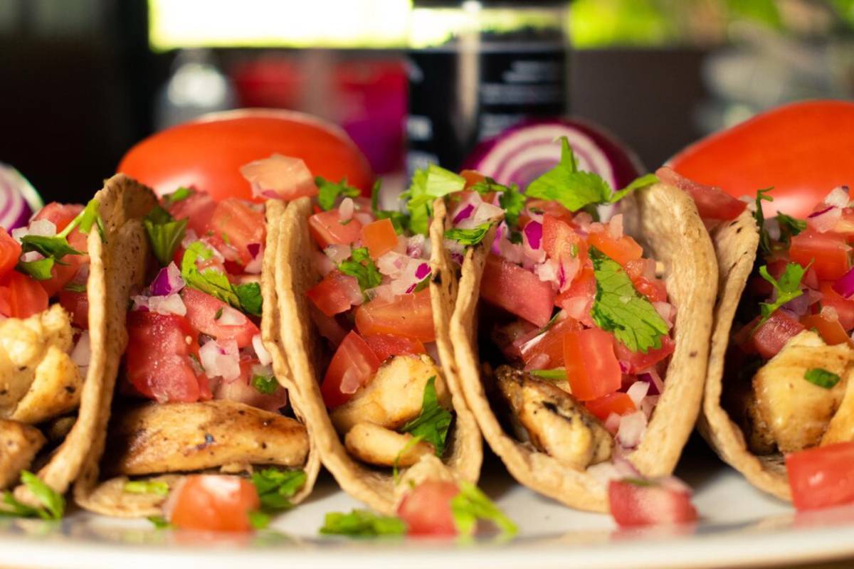 Three chicken tacos with fresh pico de gallo on a white plate.